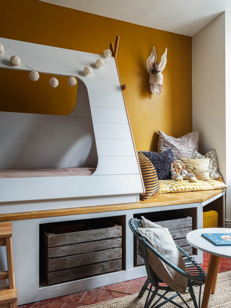 Chambre enfant avec lit cabane sur mesure, mur moutarde, caisses en bois et tomettes anciennes