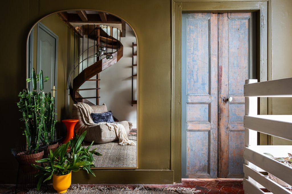 Palier avec grand miroir arche, porte ancienne patinée et mur vert olive dans une maison de caractère rénovée