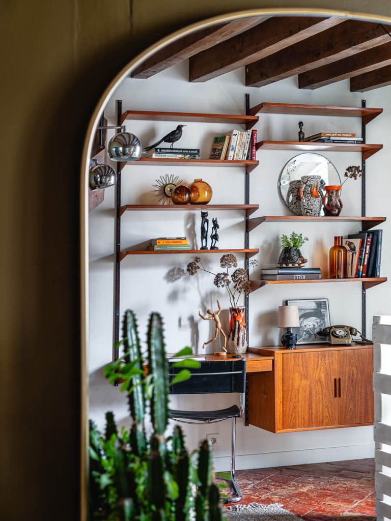 Reflet dans un miroir en arche montrant des étagères murales en bois avec objets vintage et poutres apparentes